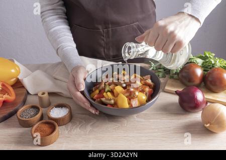 Cucinare un'insalata di verdure fresche in cucina a casa. le mani della ragazza aggiungono olio a una ciotola di insalata. vista frontale Foto Stock