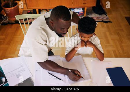 Vista ad alto angolo del padre che insegna al figlio mentre risolve problemi di matematica a casa Foto Stock