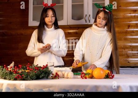 Due ragazze stanno preparando decorazioni natalizie e cibo in un ambiente festivo Foto Stock