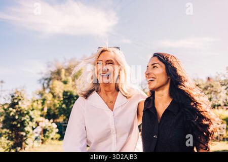 Donna anziana felice che cammina con il braccio intorno alla figlia nel cortile posteriore Foto Stock