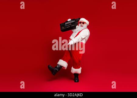 Babbo Natale con un boombox balla in uno studio rosso per un momento natalizio che cattura le vivaci vibrazioni natalizie e lo stile retrò Foto Stock
