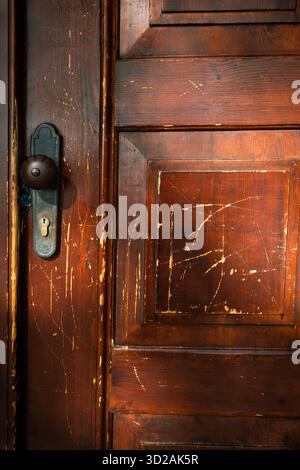 primo piano di una vecchia porta di legno graffiata con maniglia vintage che simboleggia la storia e l'architettura antica Foto Stock