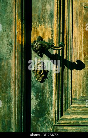 Primo piano di un'antica porta in legno verde con maniglia ornata che proietta un'ombra alla luce del sole Foto Stock