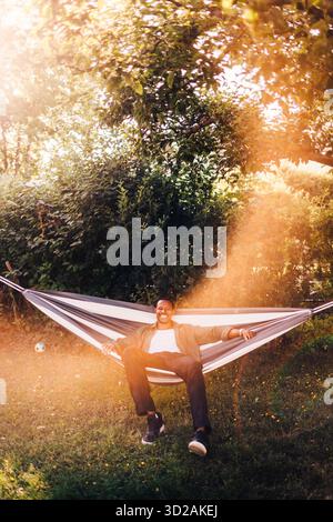Ritratto di un uomo sorridente e spensierato seduto su un'amaca in giardino Foto Stock