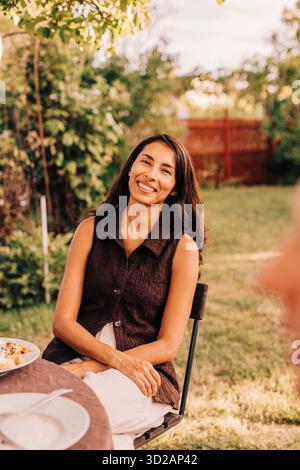 Ritratto di una bella donna sorridente seduta a tavola nel cortile posteriore Foto Stock