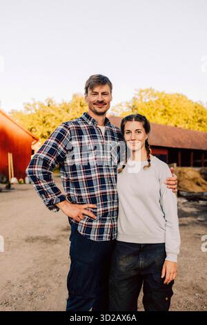 Ritratto di un agricoltore sorridente in piedi con un braccio intorno alla donna in fattoria Foto Stock