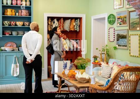 Vista posteriore di una donna che assiste la donna nell'acquisto di quadri presso un negozio di arredamento Foto Stock