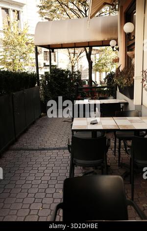 Tranquilla terrazza all'aperto con tavoli soleggiati e vegetazione, perfetta per una rilassante pausa caffè o pranzo. Foto Stock