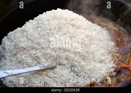 Il processo di cottura del pilaf uzbeko. Rise sta cucinando in olio in un calderone di ghisa. Cucina tradizionale uzbeka orientale, pilaf o plov con pezzi grandi Foto Stock