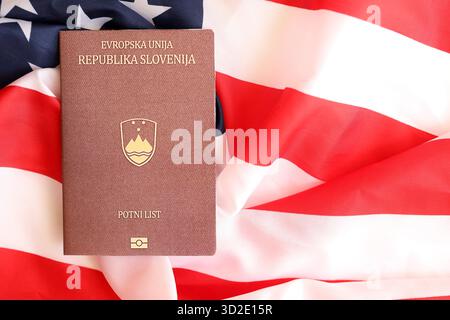 Passaporto sloveno sulla grande bandiera ondulata degli Stati Uniti d'America primo piano. Concetto di immigrazione e visto PER GLI STATI UNITI Foto Stock