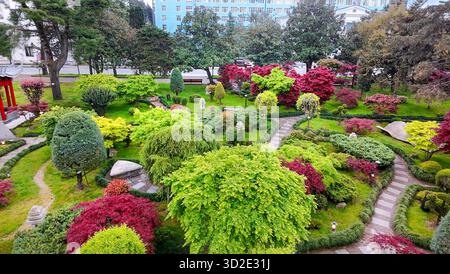 Vista droni del GIARDINO GIAPPONESE DI BATUMI con foglie rosse di aceri giapponesi (a maggio!), sentieri in pietra, lanterne e posti a sedere in pietra (o sdraiati) Foto Stock