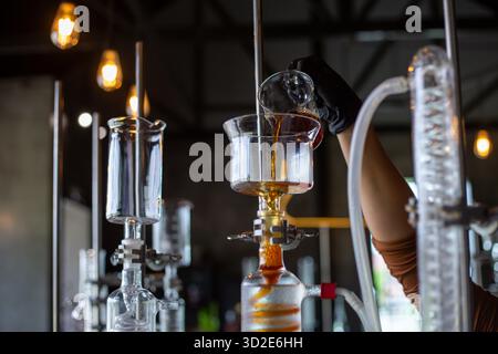 Caraffa di vetro trasparente con messa a fuoco selettiva che versa acqua di caffè in una provetta per analisi pressata a freddo. Per preparare il caffè americano freddo senza ghiaccio, i bar utilizzano s. Foto Stock