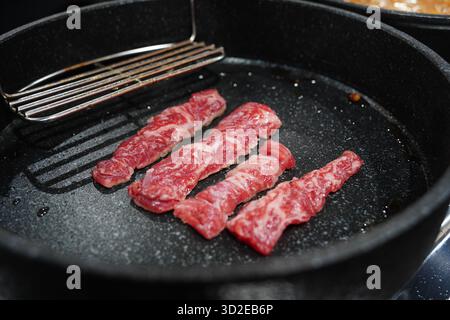 Strisce di manzo crude sfrigolanti su una padella per grill Foto Stock