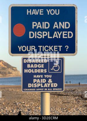 I cartelli per parcheggiare su una spiaggia di Charmouth, Regno Unito, ricordano ai visitatori di pagare ed esporre i biglietti, con una nota speciale per i titolari di badge per disabili. Foto Stock