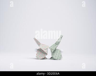 Due coniglietti origami realizzati con carta stampata sono rivolti l'uno verso l'altro su uno sfondo bianco Foto Stock