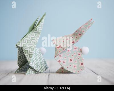Due coniglietti origami colorati su un tavolo di legno bianco con sfondo azzurro, perfetti per le decorazioni pasquali Foto Stock