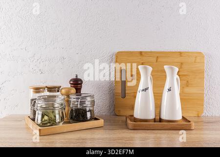 Un bellissimo vano portaoggetti per spezie in vasetti di vetro e oli in bottiglie speciali in ceramica su un ripiano in legno nello spazio cucina. Stile ecologico Foto Stock