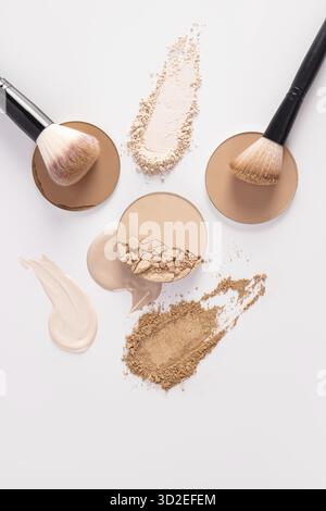 Un bellissimo sfondo cosmetico con vari tipi di polvere compatta, tratti di polvere liquida, spazzole eleganti per l'applicazione del trucco. Vista dall'alto verticale Foto Stock
