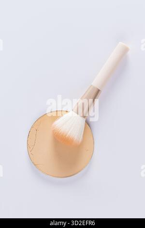 Un campione di un blocco rotondo di polvere compatta in un tono naturale e una spazzola elegante per l'applicazione del trucco. vista dall'alto verticale. layout per la progettazione Foto Stock