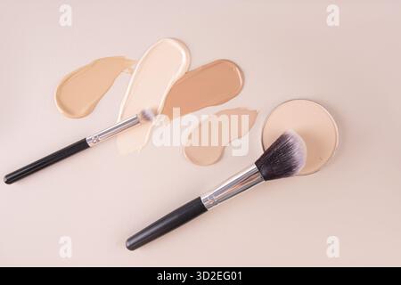 Bellissimi tratti di fondo in tonalità diverse, due pennelli per il trucco, un blocco rotondo di polvere compatta su sfondo beige. vista dall'alto. trucco Foto Stock