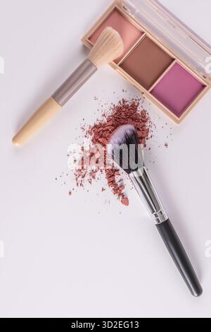 Una confezione aperta di blush multicolore, un campione della texture blush e due pennelli per il trucco su sfondo verticale bianco. vista dall'alto Foto Stock