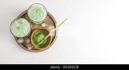 Due bicchieri con una bevanda tonificante tè-latte e cubetti di ghiaccio su un vassoio rotondo di legno. Il tè matcha è un'alternativa al caffè. Vista dall'alto, copia spazio Foto Stock