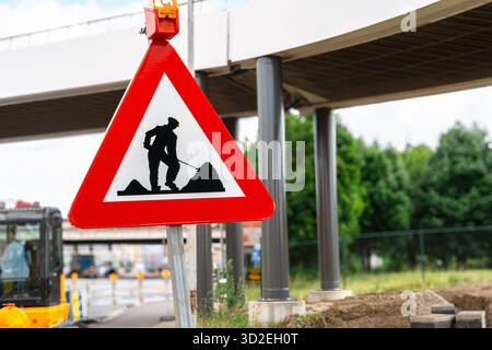 Segno rosso triangolare con silhouette di lavoratore si trova vicino a una struttura sopraelevata durante la manutenzione su strade urbane e la manutenzione urbana Foto Stock
