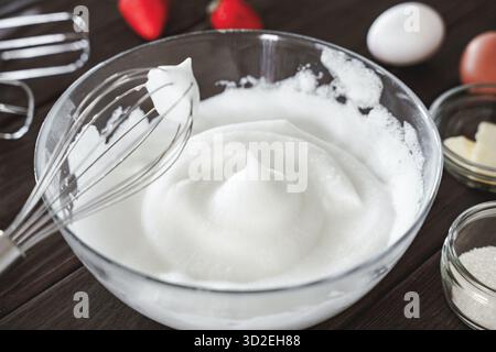Albumi freschi montati a picchi rigidi con una frusta di metallo, pronti per le ricette che richiedono schiuma ariosa e stabile come meringa o souffle Foto Stock