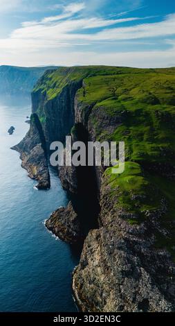 Le maestose scogliere si innalzano drammaticamente dalle tranquille acque dell'Oceano Atlantico, mostrando la lussureggiante vegetazione e l'aspra bellezza delle Isole Faroe. Lago Sorvagsvatn Foto Stock
