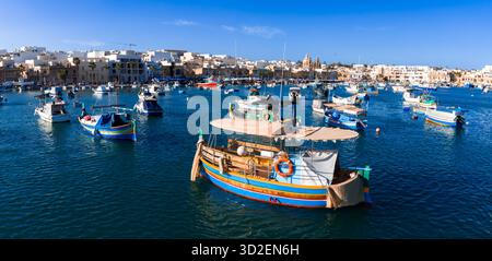 Porto di Marsaxlokk con barche luzzu e torri della Chiesa Parrocchiale a Malta Foto Stock
