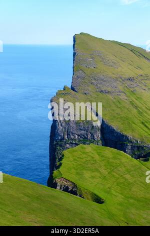 Le torreggianti scogliere di Mylingur si innalzano drammaticamente dall'oceano, mostrando lo splendido paesaggio delle Isole Faroe. La vibrante erba verde contrasta con il mare blu profondo, creando una vista mozzafiato. Foto Stock