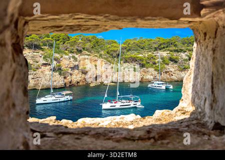 Vista segreta della spiaggia turchese sullo yachting e sulla vela attraverso la finestra di pietra, sull'isola di Maiorca. Spiaggia Cala Pi. Isole Baleari della Spagna Foto Stock