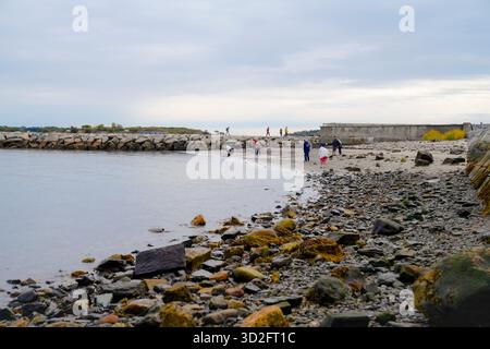 I visitatori esplorano il litorale roccioso vicino a Spring Point, camminando lungo la sabbia e il molo sotto il cielo coperto con la bassa marea in un fresco pomeriggio autunnale Foto Stock