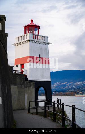 Vista laterale del faro di Brockton Point lungo il lungomare di Stanley Park, affacciato su Burrard Inlet con le montagne North Shore in lontananza. Foto Stock
