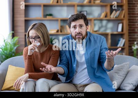 Coppia in una sessione di terapia online tesa a casa, donna che piange, uomo frustrato, discutere problemi di relazione e cercare una guida professionale tramite videochiamata. Foto Stock