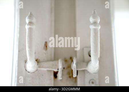 Foto macro con chiusura simmetrica vintage, dipinta di bianco, con pali ricurvi decorativi. Un dettaglio del vecchio hardware su una parete o una cornice di colore chiaro. Foto Stock