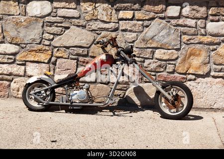 Un colpo a tutta lunghezza di una motocicletta pesantemente modificata o fatta in casa (possibilmente un mini chopper o bobber) con serbatoio rosso arrugginito e manubrio basso. Foto Stock