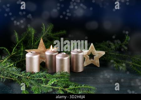 Quattro candele dorate, una accesa per il primo Avvento, stelle di legno e rami di abete su uno sfondo scuro con bokeh innevato, vacanze invernali, copia Foto Stock