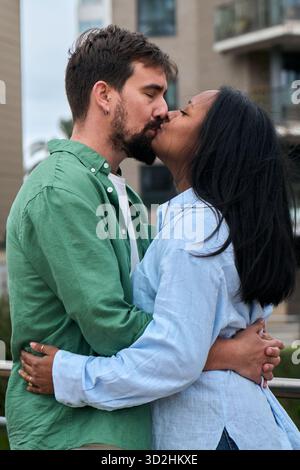 Una coppia interrazziale amorevole condivide un bacio tenero all'aperto Foto Stock