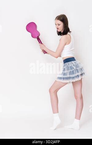 Musicista donna con ukulele in mano che oscilla strumento musicale con rabbia e irritazione, cercando di rompere ukulele in forma di disperazione ed emotiva de Foto Stock