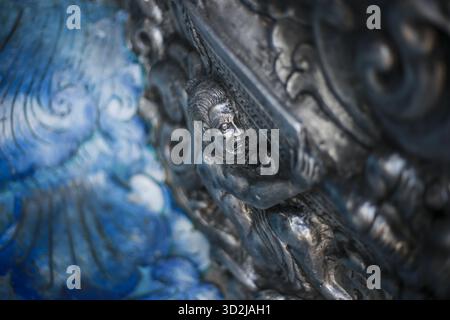 Texture metallizzata con dettagli blu. Una scultura ornata mostra motivi dettagliati e rilievi antichi e scuri, creando misteriosi e. Foto Stock