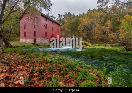 L'iconico Red Alley Spring Mill sorge accanto a una vibrante sorgente turchese, circondata dalle ricche sfumature arancioni e gialle del fogliame autunnale. Foto Stock