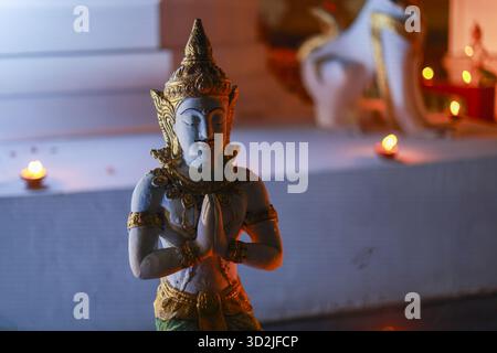 Serena statua buddista thailandese del Thepanom in posa di saluto con le mani aggrappate in preghiera. una tranquilla scultura si trova in un tranquillo tempio illuminato dal caldo, so Foto Stock
