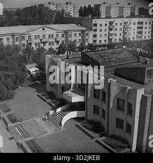 Archivio foto in bianco e nero da Sloviansk, Ucraina, luglio 1997. Questa vista ad alto angolo mostra la biblioteca centrale in Piazza della Rivoluzione d'ottobre (ora Piazza Soborna). L'edificio presenta un'architettura modernista unica in mattoni. Due donne sono sui gradini. Sullo sfondo ci sono vecchi edifici dell'epoca Stalin e nuovi blocchi di appartamenti sovietici, circondati da alberi estivi. Questo cattura il paesaggio urbano di una città post-sovietica. Foto Stock