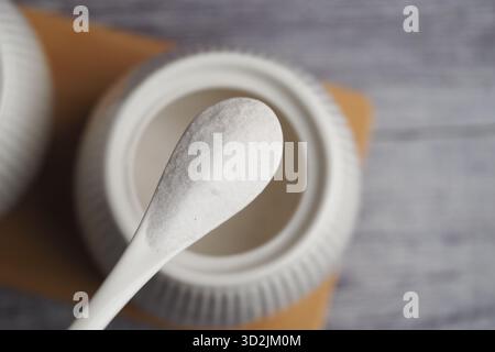 Zucchero bianco su un cucchiaio accanto a un contenitore su un tavolo Foto Stock