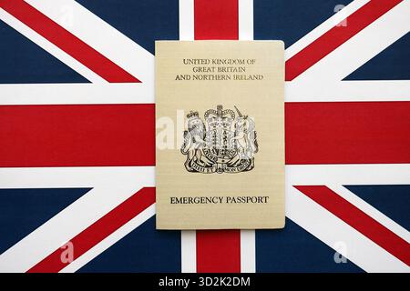 Passaporto d'emergenza britannico. Documento temporaneo di colore giallo su primo piano sullo sfondo della bandiera Foto Stock