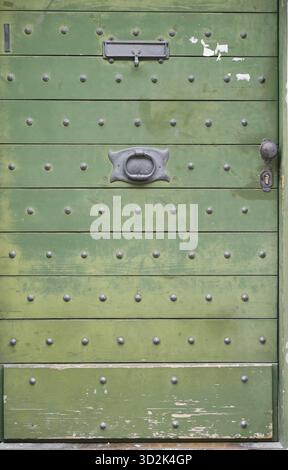 Porta in legno verde realizzata in tavole orizzontali, decorata con rivetti in metallo distanziati uniformemente, una fessura per posta, una manopola centrale e una maniglia decorativa con foro a chiave Foto Stock