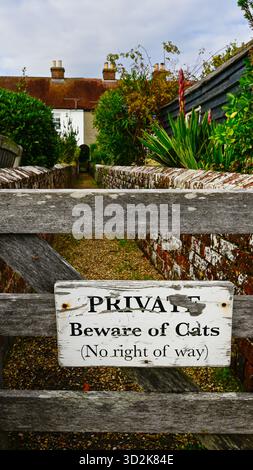 “Privato – attenzione ai gatti (No Right of Way)” su un cancello di legno tra case a schiera a Bosham, West Sussex, Inghilterra, in un giorno d’autunno coperto Foto Stock