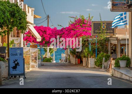 Panormos, Creta, Grecia - 2 settembre 2025: Strada con bouganville rosa in fiore e vista sul Mar Mediterraneo in un'atmosfera da villaggio greco. Foto Stock