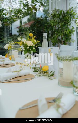 Disposizione del tavolo con eleganti decorazioni floreali e al limone con composizioni floreali gialle e bianche, accenti al limone e stoviglie ben posizionate Foto Stock